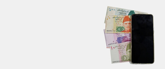 Pakistani currency bank notes aligned with mobile phone vertically in sequence 10 20 50 100 500, Pakistan State Bank official currency notes 2024 isolated on a white copy space background