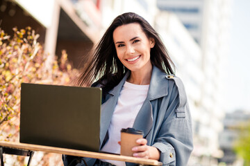 Photo of cheerful pretty lady dressed grey jacket smiling sitting cafe typing emails modern device...