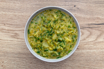 Cabbage soup made from young cabbage with parsley served in a plate, lying on the table.