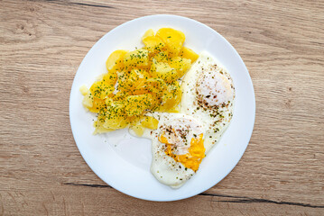 Two hard-boiled fried eggs with potatoes lying on a plate on the table.