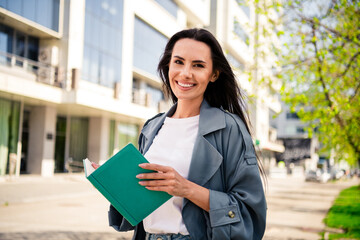 Fototapeta premium Photo of shiny attractive lady dressed grey coat reading novel enjoying good weather outdoors town street