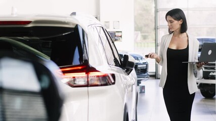 In a modern car showroom, a female consultant reviews data on her laptop, surrounded by stylish vehicles. Her expertise ensures clients receive the best advice for their automotive needs.