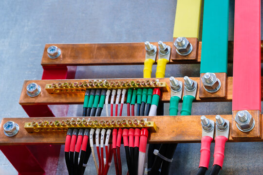Many power electric wires multi-colored wires and nuts connected to copper metal busbars electric three phases of high industrial voltage. Electricity and power supply industrial concept background
