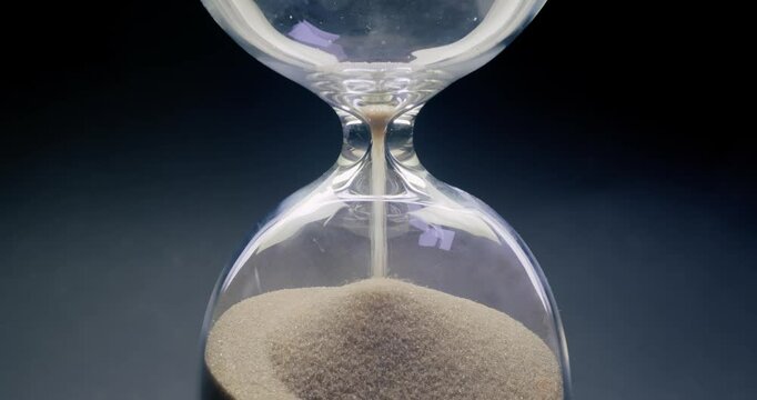 Concept of turning back time. Hourglass with grains of sand on a dark background.
