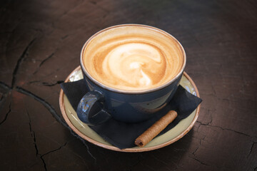 Steaming cup of cappuccino coffee with latte art on wooden table