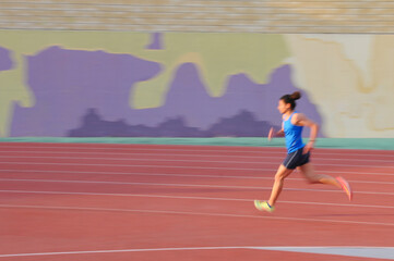 Fototapeta premium Young female athlete running on track with motion blur