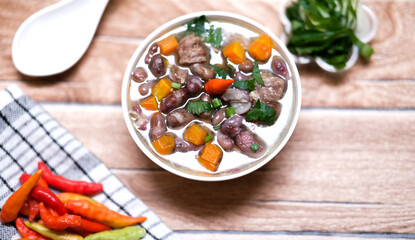Sup daging kacang merah, clear soup with beef slices, red bean and vegetables. Served in bowl on wooden background. Selected focus.