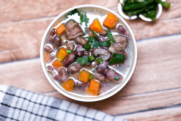 Sup daging kacang merah, clear soup with beef slices, red bean and vegetables. Served in bowl on wooden background. Selected focus.