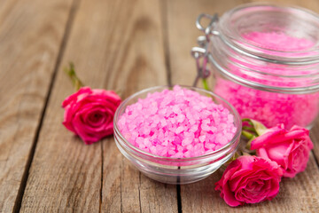 Sea salt for bath with aroma and rose flowers on textured wooden background. Pink sea salt. Spa treatments. Natural salt with herbs and essential oils. skincare concept. Meso for text. Copy space