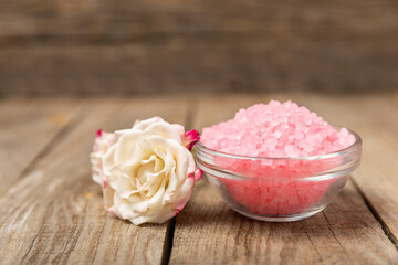 Sea salt for bath with aroma and rose flowers on textured wooden background. Pink sea salt. Spa treatments. Natural salt with herbs and essential oils. skincare concept. Meso for text. Copy space
