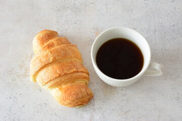 a cup of coffee next to a croissant top view