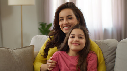 Happy family portrait smiling Caucasian woman female mother mom hug embracing cuddle joyful little girl kid preschool daughter parent and child looking camera indoors apartment room. Adoption custody