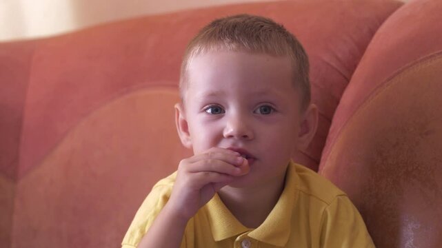 Child sits on sofa and eats food, sausage close-up