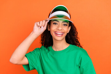 Naklejka premium Photo of young attractive american girl touching her new green stylish summer cap enjoying vacation isolated on orange color background
