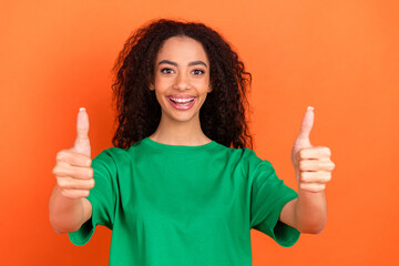 Photo of young funky attractive american girl wearing green casual t shirt enjoy symbol two thumbs up isolated on orange color background