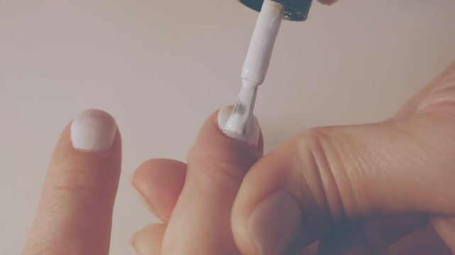 Manicurist painting her client's nails. Professional manicurist applying white nail polish to young girl's nails.