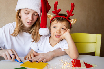 Merry Christmas. Happy New Year. Teen sister in Santa hat with little boy brother making gifts.