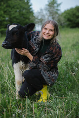 Young female farmer with a small calf in a meadow in the countryside.