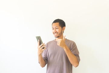 Young Asian men with purple t-shirt is holding his smartphone with happiness and smile. Positive reaction