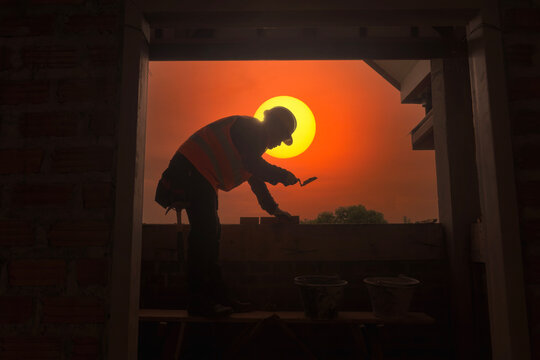 Silhouette of a bricklayer laying bricks at sunset, Thailand