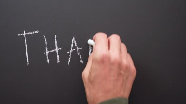 A hand writes the words or expression &ldquo;thanks&rdquo; with white chalk on a black board