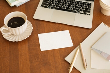 Cup of black coffee on a table next to an open laptop computer, blank card and assorted stationery