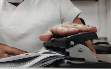 A man is stapling several sheets of paper in a modern office, sitting at a desk with office equipment around. The image captures a professional and organized work environment.