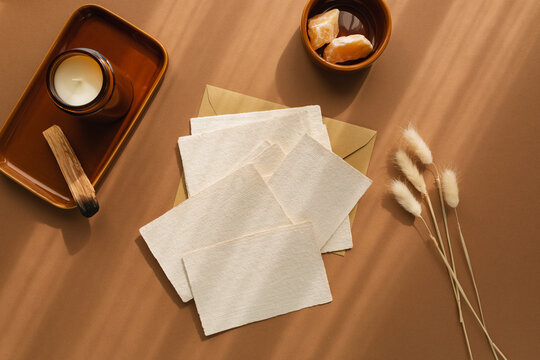 Overhead view of assorted pieces of blank cards on an envelope with hare's tail grass (Lagurus) and a candle on a wooden table