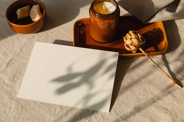 Blank piece of card on a table in sunlight with a candle on a ceramic tray