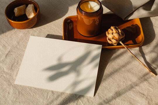 Blank piece of card on a table in sunlight with a candle on a ceramic tray