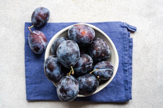 Overhead view of a Bowl of organic ripe black plums on a folded napkin