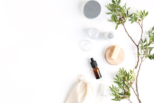 Overhead view of glass cosmetic bottles, a brown glass cosmetic dropper bottle for face serum or oil and pistachio branches on a white background