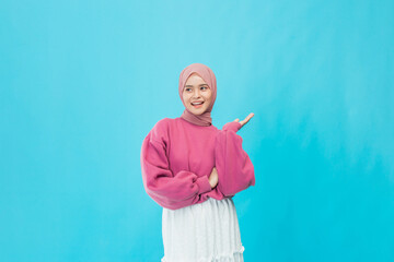 A joyful woman in a pink sweater poses playfully in front of a bright blue backdrop.