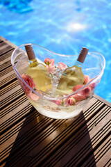 Champagne bottles in ice bucket with flowers by swimming pool.