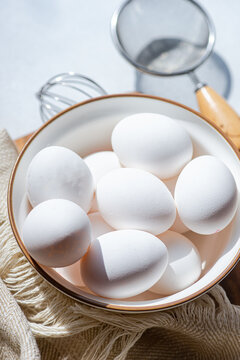 Overhead view of a bowl of white eggs with a metal whisk and sieve
