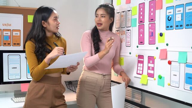 Collaboration between two female web designers focuses on a user interface design project in an office setting, highlighting teamwork and creative brainstorming