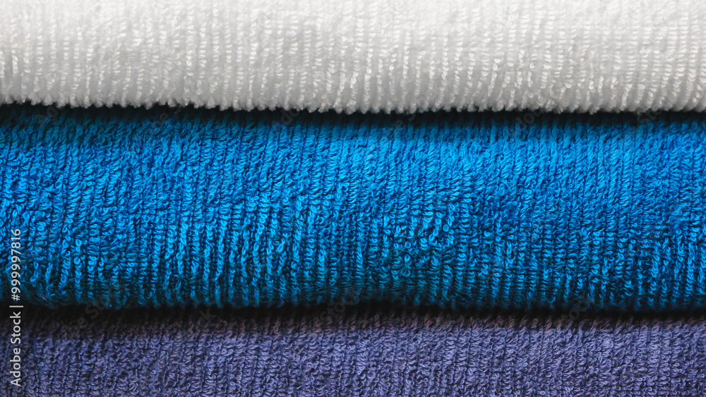 Poster multi-colored textile towels lie in a stack on a shelf