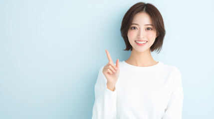 portrait of a young Japanese woman in her late 30s with short hair, wearing a white, smiling and pointing with her index finger on a plain background.