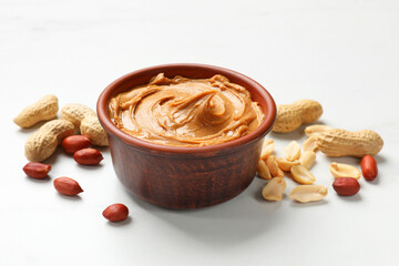 Tasty peanut butter in bowl and groundnuts on white table