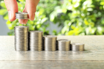 Salary concept. Woman putting coins on stack at grey table, closeup