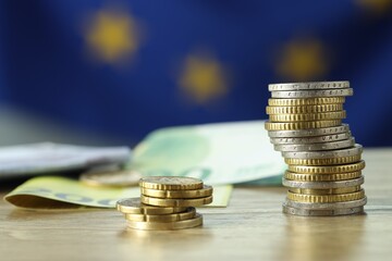 Coins and euro banknotes on wooden table, closeup