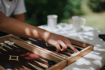 Close-up of a hand playing backgammon outside, depicting a tranquil and enjoyable leisure activity with a relaxed atmosphere.