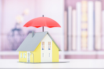 Protection from mortgage foreclosure and land contract forfeiture, business mortgage loan and real estate property insurance concept : Red umbrella covers or protects a residential home model.