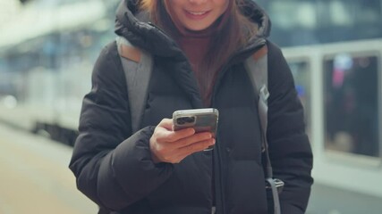Closeup - Happy woman using smart phone while waiting on station platform, Female using mobile phone at train station, Enjoying travel concept