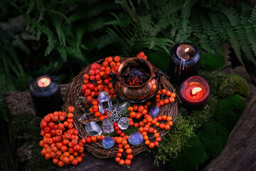 black candles, crystals, witch cauldron, amulet, rowan tree berries in forest. Magic, Witchcraft,...