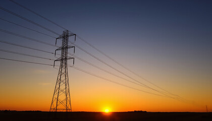 High voltage over head power line tower in an open field at sunset background.
