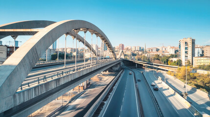 Modern arched steel bridge with pedestrian access and cityscape under clear blue sky during daytime