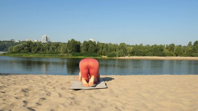 Young sports gymnast woman doing headstand on exercise mat on beach. Summer water workout. Complex yoga exercise
