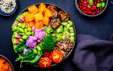 Vegan vegetarian buddha bowl with pumpkin, quinoa, tomatoes, spinach, celery, edamame, tofu, broccoli and seeds, black background, top view