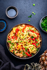 Stir fryed noodles with chicken slices, pineapple, red paprika, onion, soy sauce, garlic, ginger and sesame seedsl. Black background, top view